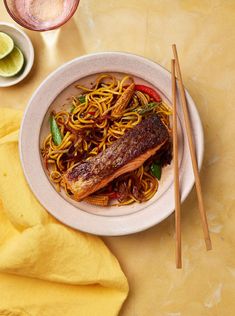 a white plate topped with fish and noodles next to chopsticks on a table