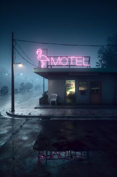 a motel sign lit up in the dark on a foggy night with chairs outside