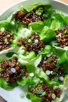 lettuce leaves with meat and seasoning on top, sitting on a white plate