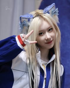 a girl with long blonde hair and blue ears making the peace sign