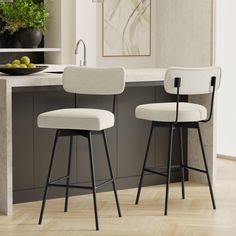 two white bar stools sitting in front of a kitchen island with fruit on it