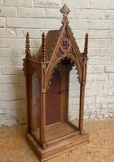 an old wooden grandfather clock with carvings on the front and sides, sitting against a white brick wall