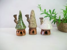 small clay houses are lined up next to a potted plant