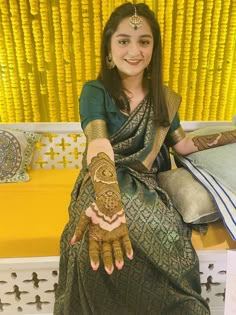 a woman sitting on a bench with her hands painted in hendi and bracelets