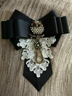 an owl brooch is attached to a black tie with white lace and pearls on it