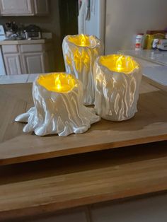 two white candles sitting on top of a wooden table next to a refrigerator freezer