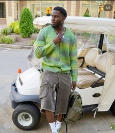 a man standing next to a golf cart with a bag on his shoulder and wearing sneakers