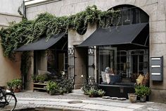 an old photo of the outside of a building with potted plants and people sitting on benches