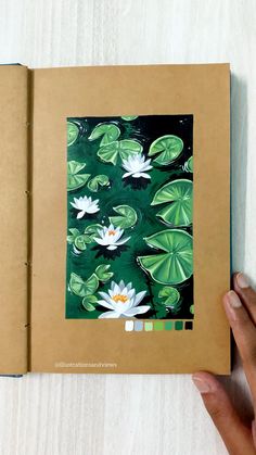 a hand is holding an open book with water lilies and leaves on the pages