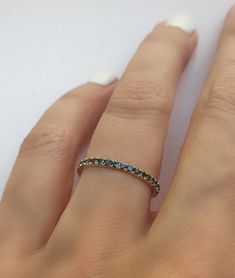 a woman's hand wearing a gold ring with blue and green stones on it