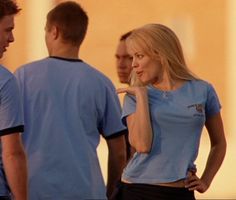 two men and a woman are talking to each other in front of a man who is wearing a blue shirt