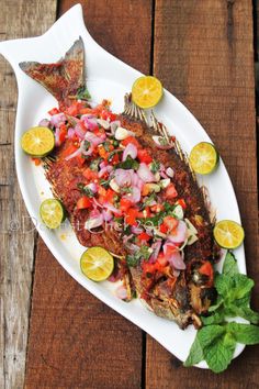 grilled fish with tomatoes, onions and limes on a white platter