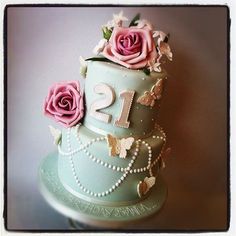 a three tiered cake with pink roses and pearls on the top is decorated in blue frosting