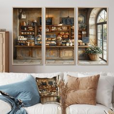 three paintings hanging on the wall above a couch in front of a coffee shop with bread and pastries