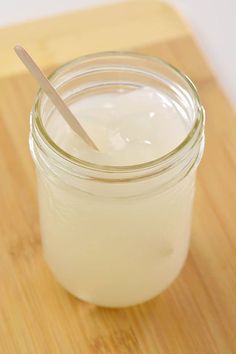 a wooden cutting board topped with a glass jar filled with liquid and a plastic spoon