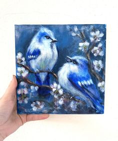 a painting of two blue birds perched on a branch with white flowers in the background