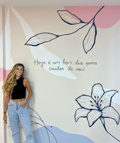 a woman standing in front of a wall with flowers painted on it and words above her