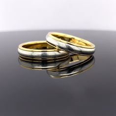 two gold and silver rings sitting on top of a black table next to each other