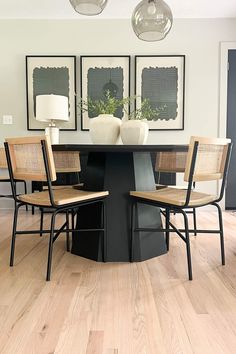 a dining room table with four chairs and two pictures on the wall above it that have plants in them