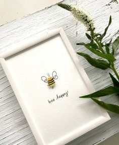 a white frame with a bee on it next to some flowers