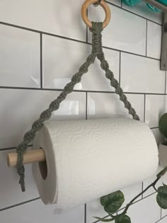 a roll of toilet paper hanging from a hook on a wall next to a potted plant