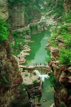 people are standing on the edge of a cliff overlooking a river and waterfall with green water