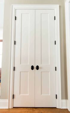 two white doors with black knobs in the middle of an empty room and wood flooring