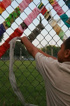 a young boy hanging ribbons on a chain link fence