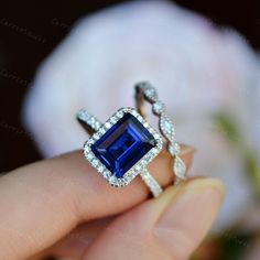 a woman's hand holding an engagement ring with a blue stone surrounded by diamonds