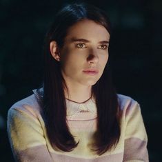 a woman with long hair wearing a sweater looking at the camera while standing in front of a dark background