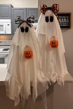 two white ghost decorations with orange pumpkins and black bows on their heads are hanging from the kitchen counter