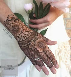 a woman holding a bouquet of flowers with henna tattoos on her arm and hand