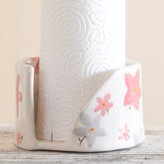 a white toilet paper holder with pink flowers on it and a roll of toilet paper next to it