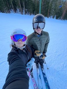 two people standing in the snow with skis and goggles on their hands,