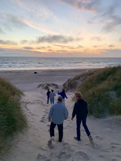 several people are walking on the beach towards the water and sand dunes at sunset or dawn