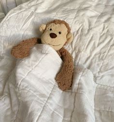 a teddy bear wrapped in a blanket on top of a white comforter with a brown nose