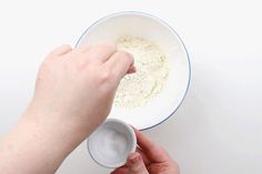 a person holding a white bowl with food in it and another hand reaching for something