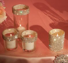 some candles are sitting on a table with pink cloth and flowers in vases next to them