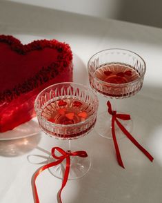 two heart shaped glasses are next to a valentine's cake