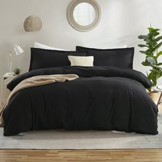 a bed with black comforter and pillows in a room next to a potted plant