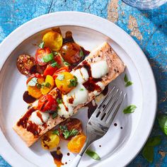 a white plate topped with fish covered in sauce and veggies next to a fork