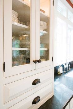 a kitchen with black counter tops and white cabinets in front of a window that has glass doors