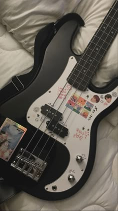 a black and white bass guitar with pictures on it's body, laying on a bed