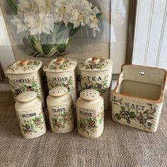 four ceramic jars with flowers in them sitting on the floor next to a painting and vase