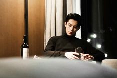 a man sitting at a table with a wine glass in front of him and looking at his cell phone