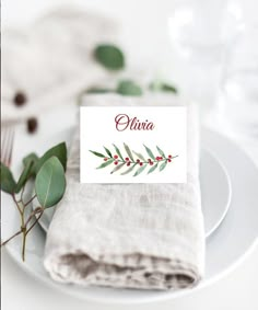 a place card is placed on a white plate with eucalyptus leaves and greenery in the background