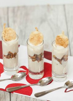 three desserts are sitting on a red and white tablecloth with spoons next to them