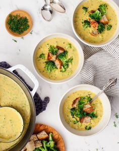 three bowls of soup with broccoli and chicken in them on a white table