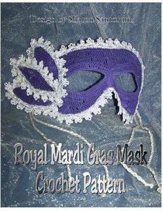 a purple and white crochet mask with lace on the bottom, sitting on a blue cloth