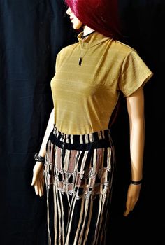 a mannequin with red hair wearing a gold top and fringe skirt, against a black background